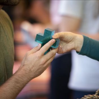 one person hands a green glass cross to a student